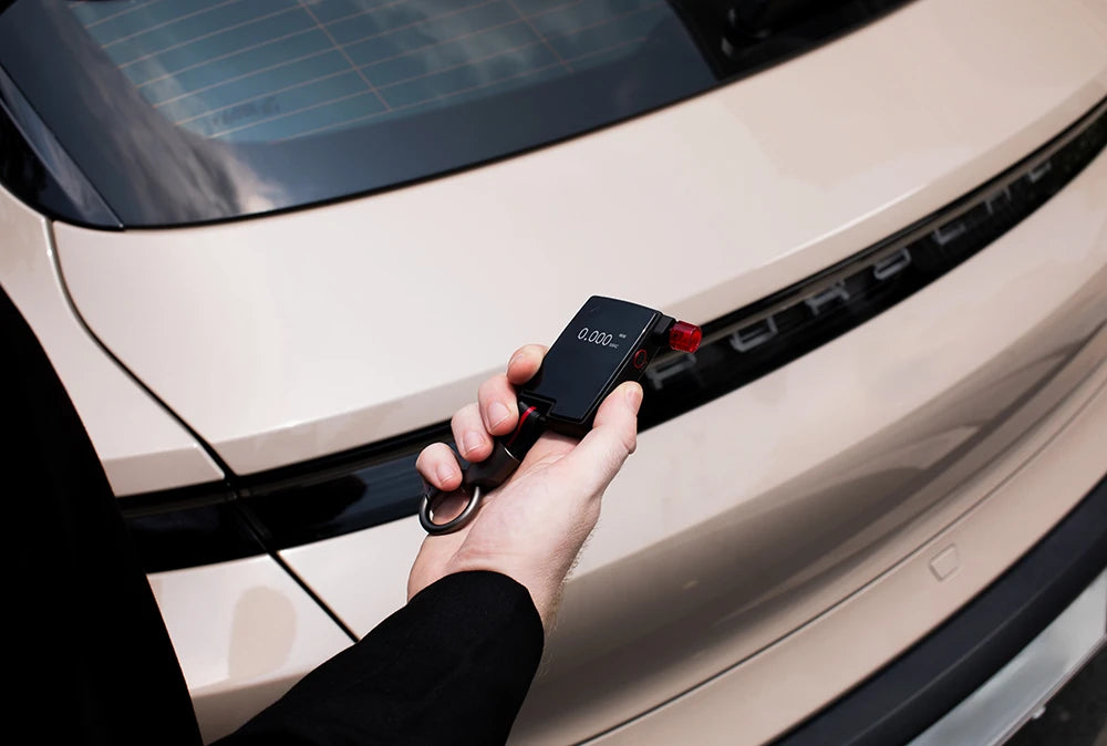 Hand holding Andatech GT Fuel Cell Breathalyser by a car
