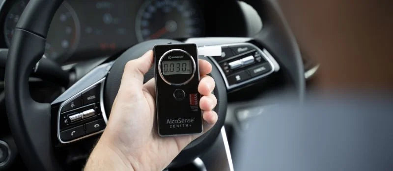 A man holding Andatech AlcoSense Zenith+ personal breathalyser in a car