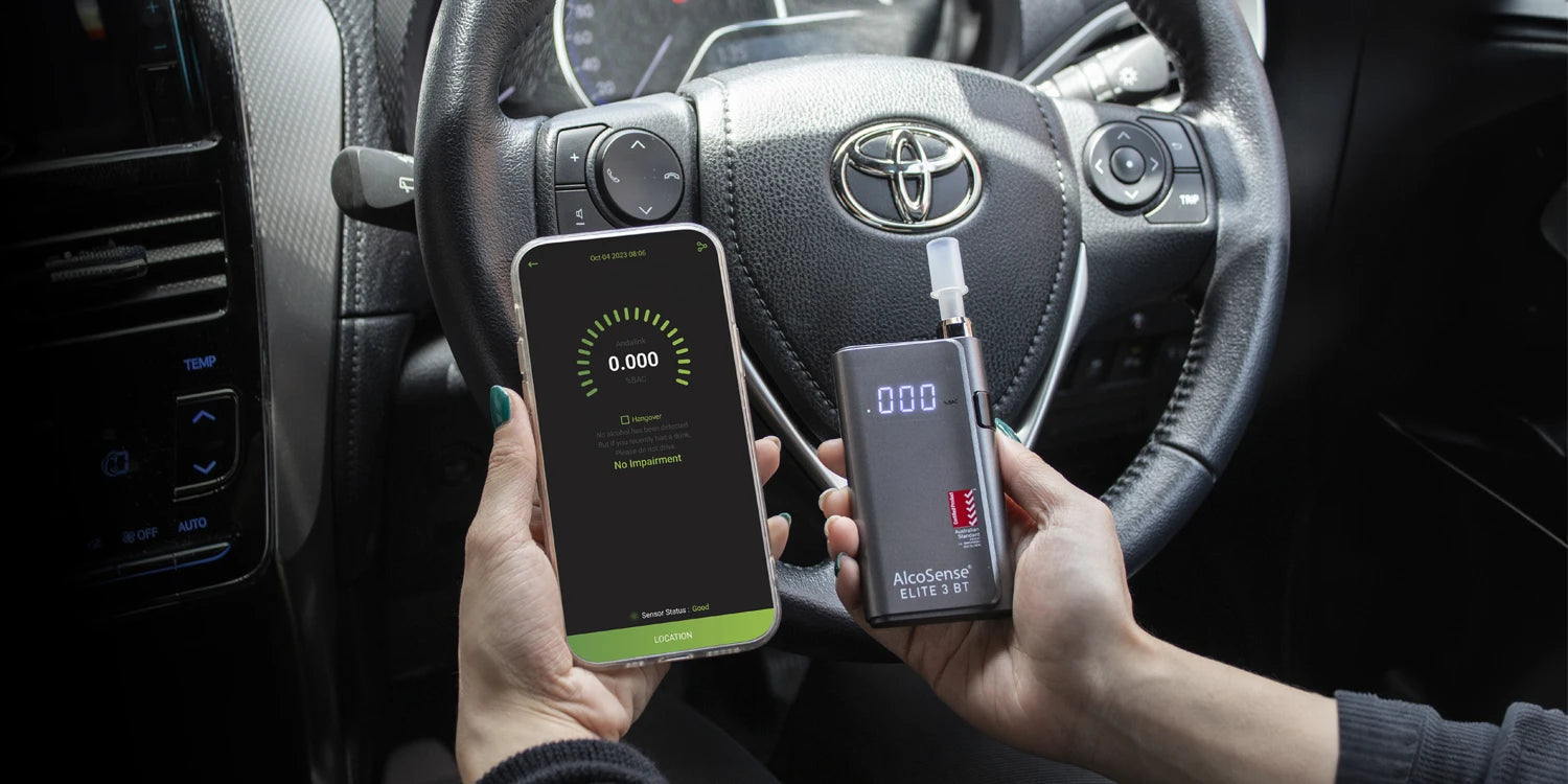 A person holding Andatech AlcoSense Elite 3 BT smartphone breathalyser in the car