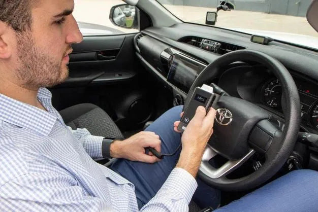 A man using the Andatech ALX3000 interlock breathalyser in his car before driving