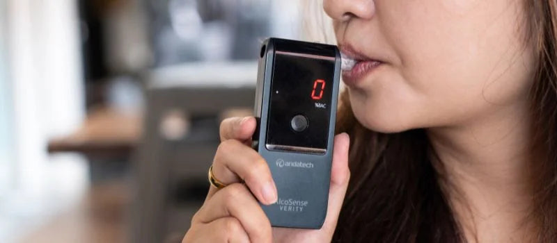 A woman blowing into the Andatech AlcoSense Verity personal breathalyser