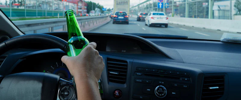 Person driving a car on a highway with beer bottle in hand